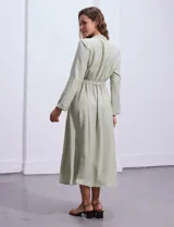 Vestido maxi color beige, con cuello mao y escote en V. Presenta mangas largas con presilla y botón para regular el largo, y un lazo ajustable en la cintura que marca la silueta.