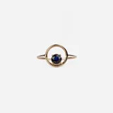 Anillo de oro 18k con diseño minimalista que presenta un zafiro azul engastado en un círculo metálico.