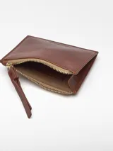 Monedero mediano de piel bovina de curtición vegetal, color rojo, con textura craquelada. Posee un compartimento principal con cierre de cremallera y un tarjetero en la parte trasera.