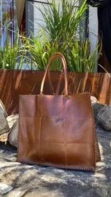 Bolso tote grande de cuero natural en color marrón, con diseño de piezas unidas mediante costuras visibles y asas de hombro.