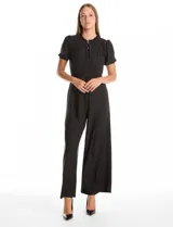 Enterito de seda fría color negro, con cuello a la base fruncido, escote en V con botones metálicos y detalle plisado vertical en el frente. Presenta mangas cortas con terminación fruncida, cintura con lazo de ajuste y pantalón de pierna ancha con caída fluida.