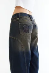 Pantalón de jean tipo balloon de tiro bajo, color marrón oscuro. Presenta un diseño con recortes curvos en las piernas, cierre frontal con doble botón en la cintura y costuras reforzadas.