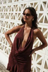 Vestido corto bordó con hilo brillante, escote halter pronunciado y detalle drapeado en el frente. Falda ajustada con fruncidos laterales y terminación con volados.