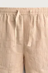 Shorts relaxed fit color beige con textura en relieve tipo jacquard, cintura elástica con cordón ajustable y detalle de bordado en contraste en el bajo.