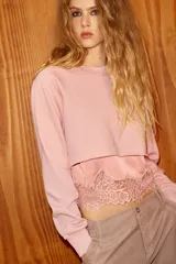 Sudadera crop de cuello redondo y manga larga con puños elásticos. Presenta un diseño de doble capa con un top interior satinado y un bajo decorado con encaje a tono.