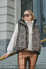 Chaleco marrón con estampado abstracto en tonos marrones y negros, con cierre frontal y broches a presión. Interior forrado con tela de peluche color crema y bolsillo interno.