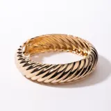 Brazalete rígido dorado con diseño acanalado en espiral.