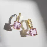 Aros dorados con forma de argolla con bisagra y pequeños brillantes engarzados. Presentan un dije cuadrado con cristal rosa.