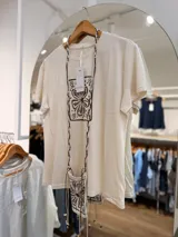 Remera de manga corta y cuello redondo color crudo, con estampado floral marrón en el frente. Incluye una mini cartera colgante a juego con el mismo diseño.