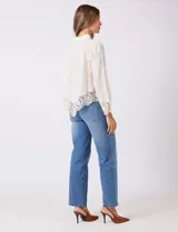 Camisa de algodón con bordado suizo, cuello con solapa y cierre frontal con botones. Presenta mangas largas con terminación de encaje calado y un ruedo asimétrico en pico con un amplio galón de encaje.