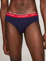 Pack de tres calzoncillos tipo slip de la marca Tommy Hilfiger, confeccionados en algodón elástico, con cintura elástica con el nombre de la marca y líneas distintivas. Incluye una unidad con cintura blanca, otra con cintura azul marino y otra con cintura roja.