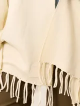 Pashmina de textura suave y color crema, con diseño liso y terminaciones en flecos en los extremos. Incluye una etiqueta decorativa en una de las esquinas.