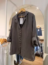 Camisa de lino gris oscuro con cuello solapa, mangas largas remangadas y cierre frontal de botones marrones.