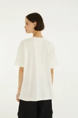 Remera blanca de algodón con cuello redondo y mangas cortas, de corte holgado. En el frente presenta el texto "Farm Rio" en tono celeste y un estampado gráfico de un tucán con anteojos de sol que reflejan un paisaje playero.
