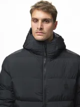Campera puffer color verde militar, con diseño capitoneado, cuello alto y capucha integrada. Cuenta con cierre frontal, bolsillos laterales con cierre y puños con ojal para el pulgar.