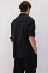 Camisa negra de manga larga con cuello clásico, tapeta con botones y bolsillo en el pecho. Corte regular.