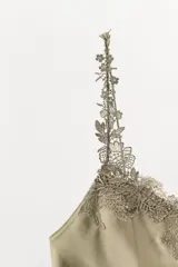 Vestido corto de satén con escote en pico y tirantes finos. Presenta delicadas aplicaciones de encaje a tono en el escote y a lo largo de la falda, con una abertura lateral en el bajo.