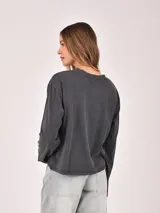 Remera de manga larga color gris oscuro con efecto gastado, corte holgado y estampado frontal con texto en color rosado.