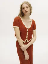 Top de tejido calado con cuello en V, mangas cortas y cierre frontal con botones carey. Presenta detalles de ribetes en color contrastante en el cuello, puños y ruedo.