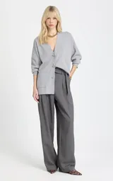Cardigan de punto color gris, de corte holgado, con escote en V profundo, cierre frontal de botones, mangas largas con puños ajustados y bolsillos delanteros aplicados.