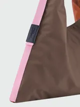 Bolso tipo hobo de gran tamaño en color verde, con detalles laterales en naranja y correa de hombro integrada. Presenta un diseño minimalista con cierre de botón a presión.