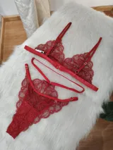 Conjunto de lencería de encaje color rojo, compuesto por un bralette triangular con breteles finos y una tanga con diseño de tiras cruzadas y detalles de encaje.