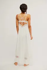 Vestido largo slip blanco de tela liviana y semitransparente, con silueta trapecio, escote cuadrado, tiras regulables, detalles de encaje, volado en el ruedo y espalda descubierta con lazo de ajuste.