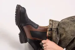 Botas estilo Chelsea de cuero color marrón, con paneles elásticos laterales negros, presillas traseras y suela chunky de goma negra con plataforma dentada.