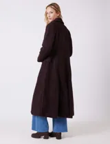 Tapado largo de bouclé color marrón oscuro, con silueta entallada que termina en evasé. Tiene cuello de solapa amplia, cierre frontal con tres botones a tono y bolsillos funcionales con solapa. Incluye forro interno a tono.