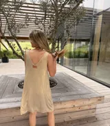Vestido corto sin mangas en tono dorado, con cuello en V de cuero con detalles cortados y bordados a mano.