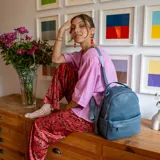 Mochila de tamaño mediano en color amarillo, confeccionada en símil cuero. Presenta un compartimento principal con cierre metálico, un bolsillo frontal con cierre y broche, y bolsillos laterales. Incluye correas regulables para la espalda, asa de mano y una correa adicional para llevar al hombro.