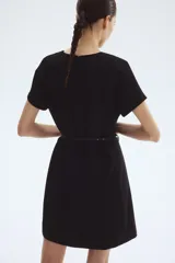 Vestido corto negro, de corte entallado, con cuello redondo y mangas cortas raglán. Incluye un cinturón fino con hebilla metálica decorativa.