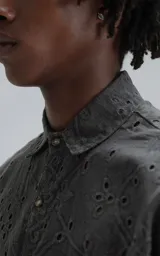 Camisa de manga corta con calce oversize, confeccionada en algodón con bordado tipo broderie y acabado con efecto desgastado. Presenta cuello clásico y cierre frontal con botones.