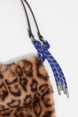 Bolso de hombro con estructura blanda, confeccionado en poliéster con acabado de pelo largo en color beige. Presenta asas de cuero marrón y detalles de cordones trenzados. Incluye cierre de cordón y bolsillo interior.