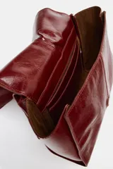 Bolso formato mini shopper de piel con acabado brillante y efecto arrugado. Cuenta con doble compartimento, cierre mediante botón imantado, bolsillo interior y asa de hombro ajustable.