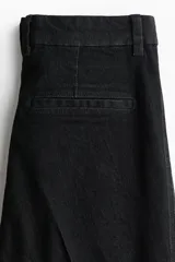 Jean de tiro alto con corte acampanado desde la rodilla, confeccionado en denim suave con leve elasticidad. Presenta cierre frontal con botón, bolsillos traseros insertados y costura central marcada en las piernas.