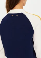 Campera bomber azul marino con mangas color crema con rayas mostaza. Tiene cuello, puños y ruedo acanalados, cierre frontal con botones a presión y corte holgado.