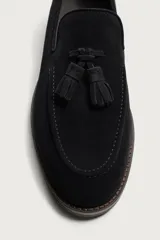 Mocasín de vestir negro confeccionado en piel con acabado serraje, con detalle de borlas en el empeine y ligero tacón.