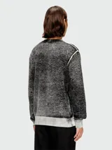 Buzo de punto con textura jaspeada en tonos gris y negro, cuello redondo y mangas largas con puños en contraste. Presenta costuras expuestas en los hombros.