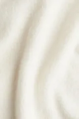 Chaleco corto de punto suave color blanco hueso, con cuello camisero y tapeta de tres botones oscuros. Presenta ribete acanalado en sisas y bajo.