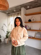 Campera de estilo safari en color beige, confeccionada en material tipo napa. Presenta cuello alto, cierre frontal con botones metálicos, bolsillos frontales con solapa y detalles de trabillas en los puños.