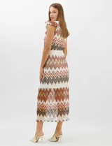 Vestido midi confeccionado en tejido de punto calado, con patrón geométrico en zigzag en tonos blanco, marrón, tostado y azul. Presenta escote a la base, mangas cortas con volados en los hombros, silueta recta y forro interior a tono. Incluye un cinturón fino con hebilla metálica.