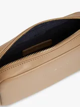 Cartera bandolera de poliuretano color beige, modelo Essential de Tommy Hilfiger, con diseño compacto de líneas redondeadas, cierre de cremallera e inscripción de la marca en bajo relieve en el frente. Cuenta con una correa cruzada ajustable de jacquard tonal.