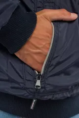 Campera de nylon color azul marino con cierre frontal completo, capucha desmontable y puños elásticos. Presenta bolsillos con cierre y logo aplicado en la manga.