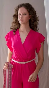 Mono fucsia con escote en V, mangas cortas con volados, cintura elastizada y cinturón fino blanco.