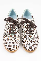 Zapatillas de estilo running con estampado animal print de leopardo sobre fondo blanco. Presentan detalles en piel verde tornasolada en la parte trasera y lengüeta, cordones oscuros y suela de goma dentada con cuña interna.