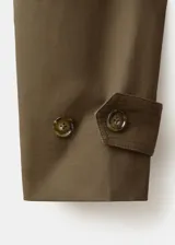 Chaqueta de gabardina color verde militar, de corte oversize con cuello alto abotonado de manera asimétrica, mangas largas con puños ajustables y cinturón ajustable del mismo tejido.