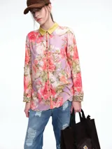 Camisa de silueta relajada con estampado floral en tonos rosas y violetas. Presenta cuello camisero en color amarillo mostaza, cierre frontal con botones, y puños con detalle de estampado animal print. El ruedo tiene un acabado festoneado.