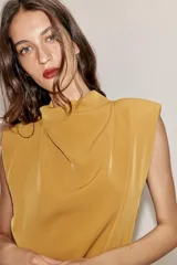 Vestido corto color mostaza con cuello fluido, manga sisa y hombreras marcadas. Presenta un detalle de lazada en la cintura y cierre de cremallera oculto en la espalda.