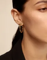 Aros de metal bañados en plata, de diseño abierto con forma de argolla y una pequeña barra perpendicular en la parte superior.